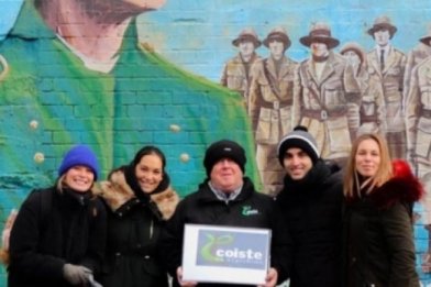Group of People with Coiste Tour Guide at the back of them Mural with Irish Political Theme 