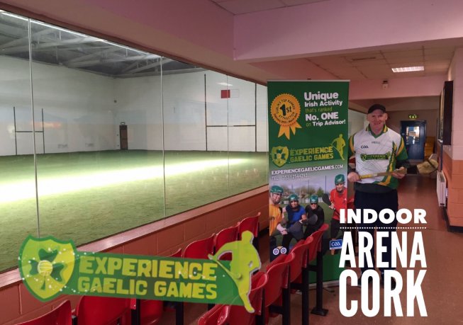 Sports venue with Man standing wearing players kit and big overlay texts Experience Gaelic Games Indoor Arena in Cork - view from the viewing gallery