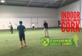 Hurling Match on Indoor Pitch  Players in a kit and big overlay texts Experience Gaelic Games  and Indoor Hurling in Cork