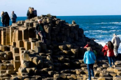 Group of students standing on basalt pillars of Giant's Causeway on a sunny day with Atlantic Ocean in the background