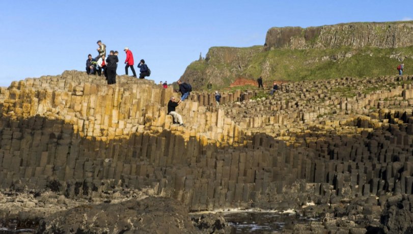 Group of people during low tide on a Giant's Causeway basalt columns - view towards cliffs on the east side