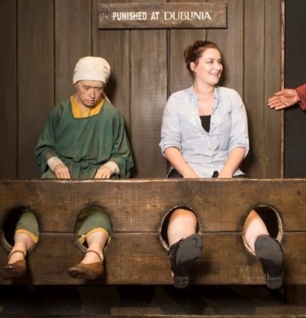 Mediaeval stocks women visitor sitting with legs in stocks next to the medieval women mannequin model - exhibition