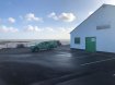 Car park with a green pick up car on the front of the Gaelic games club house sea shore at the background 