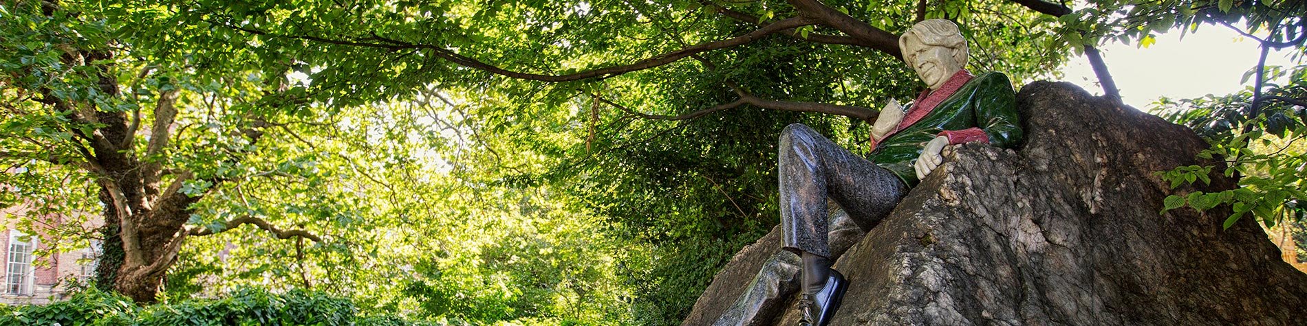 The Oscar Wilde Statue under the shadow of tall trees