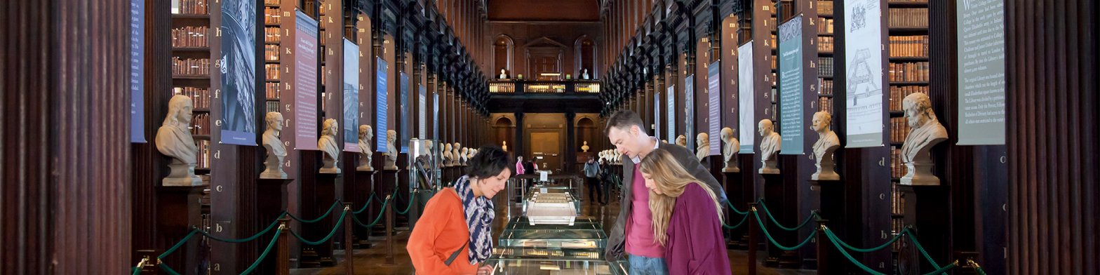 A family looks at displays at Trinity College Library whilst busts of famous historical figures line the walls either side of them.