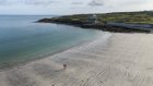 Bird ey view of a beach with two people walking on the sand further coastal cliffs and a sea