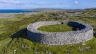 Tourist visiting circular small fort with thick stone made wall standing in the middle of the field with a sea view on the horizon