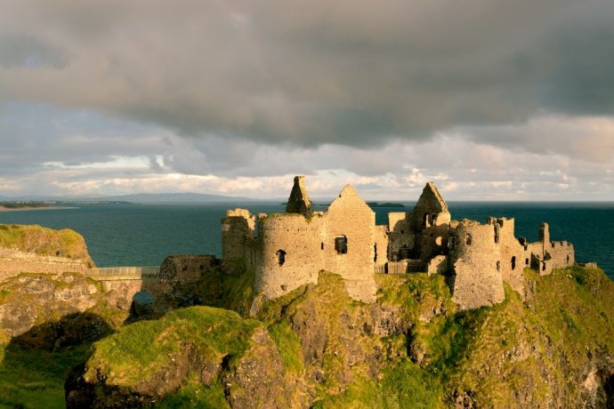 Sunrise Brightens Walls of Dunluce Castle in Ireland with Heavy Grey Clouds Above the Ruin 