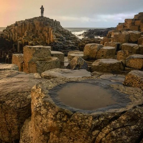 Close up view of the puddle at the top of the basalt column in the UNESCO Heritage site - Giant's Causeway During Sunset in Co Antrim with a person standing at the top of one of the basalt hills of the costal geo park 