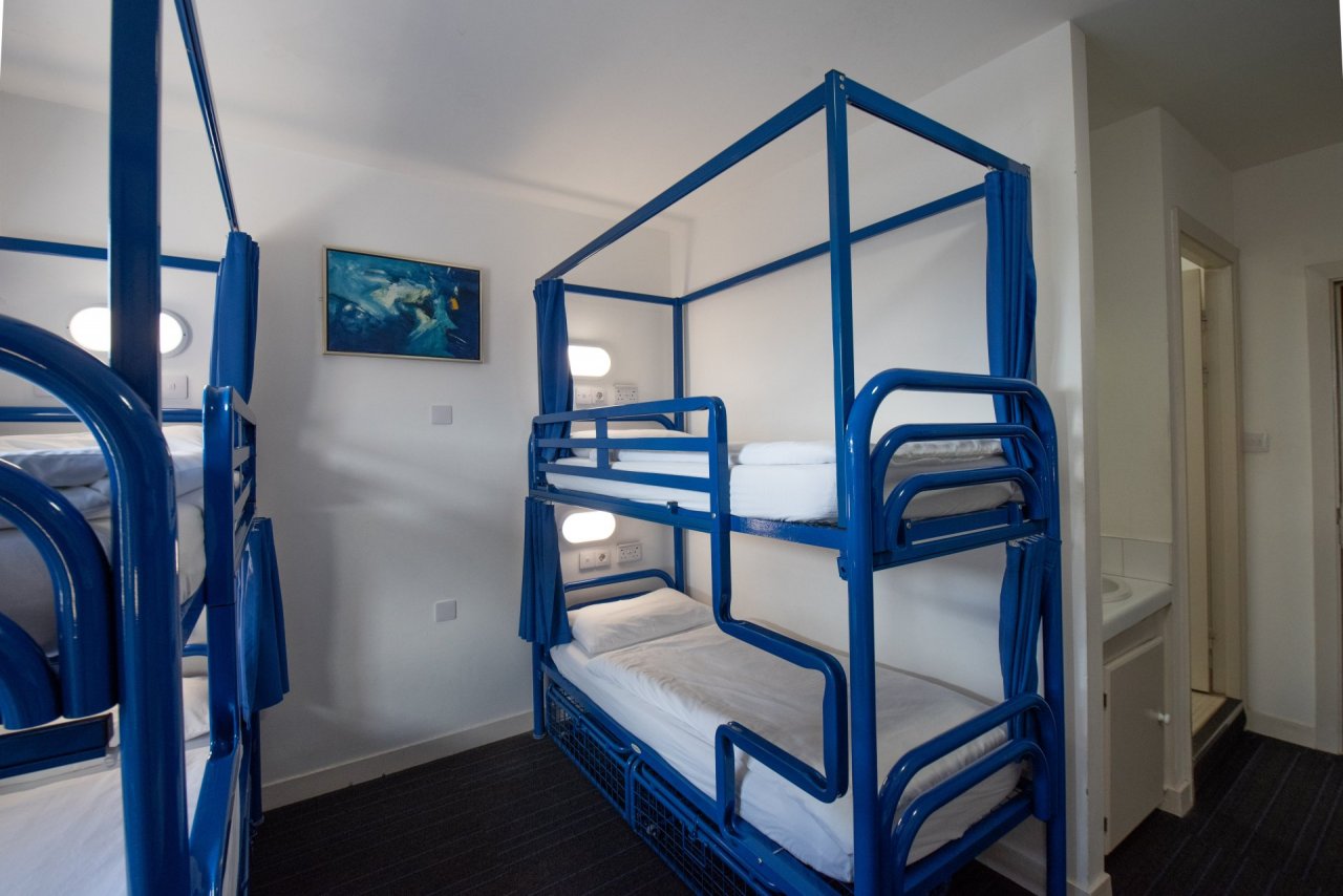 Two Blue Bunk Beds with Individual Lights and Privacy Curtain in Hostel Room
